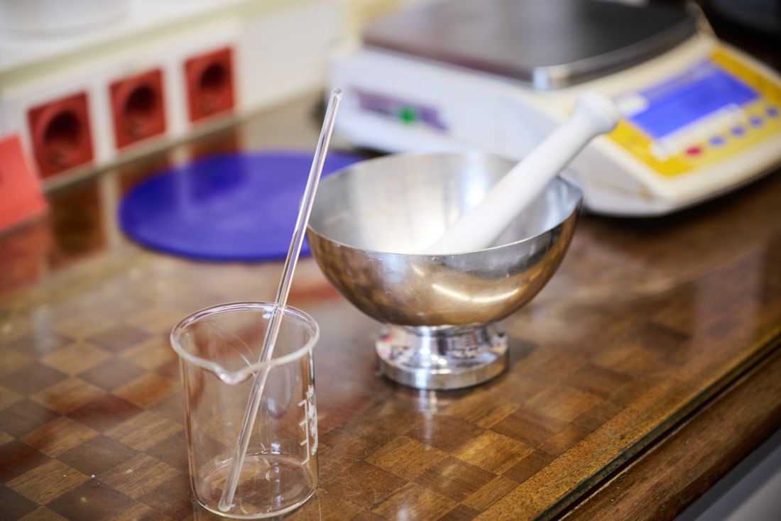 Mörser, Becherglas und Glasstab auf dem Rezepturtisch, im Hintergrund eine Waage